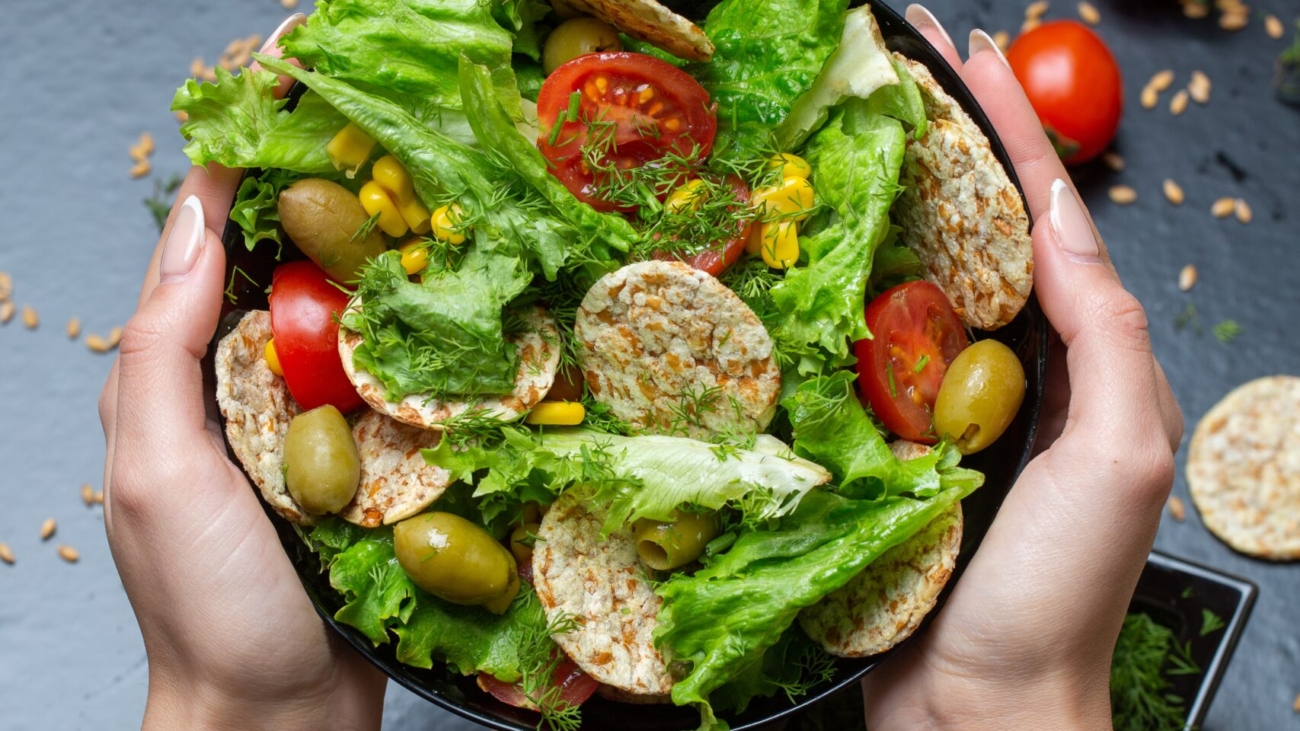 A vertical closeup of a person holding a bowl of salad with crackers and vegetables under the lights