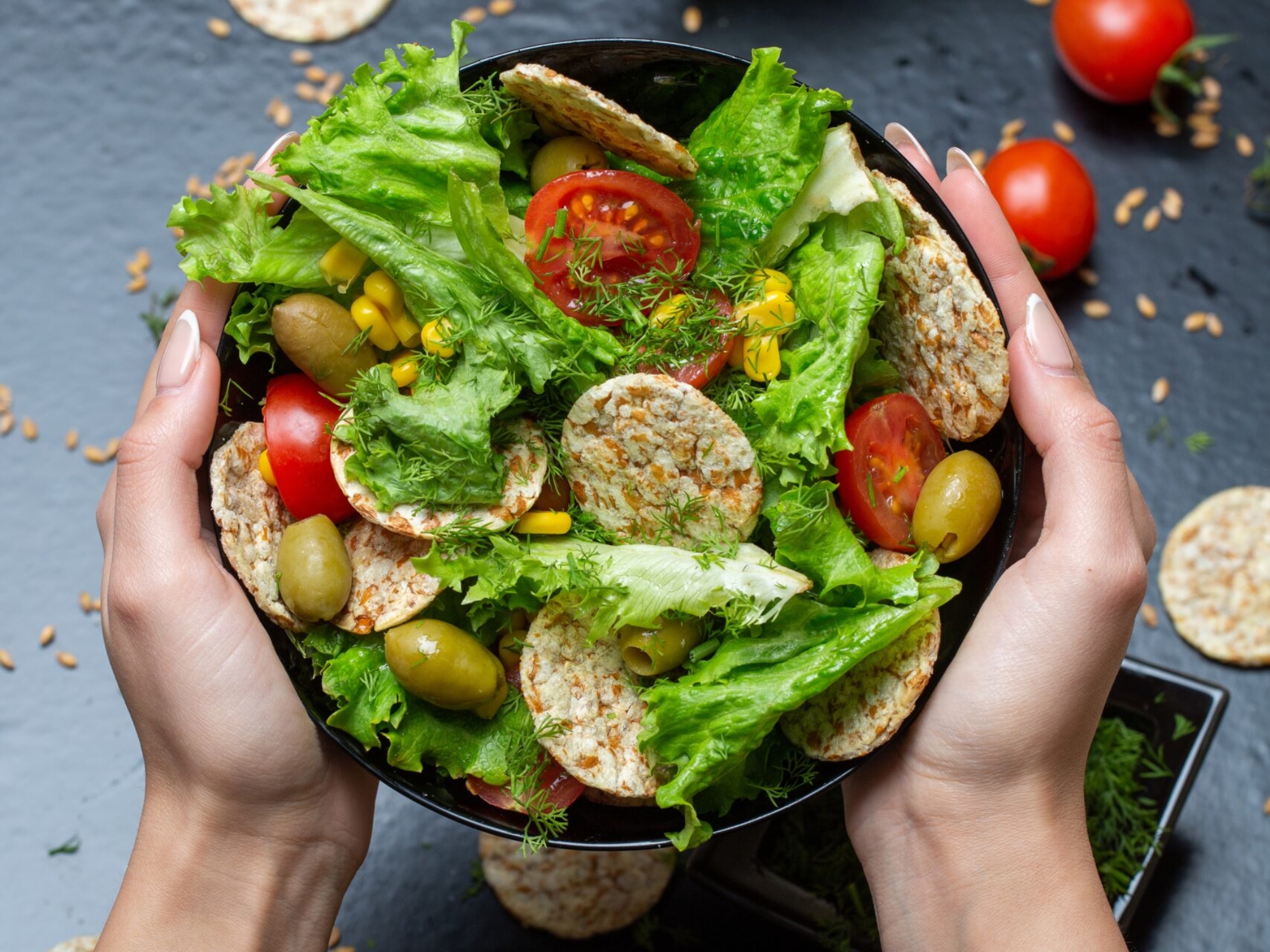A vertical closeup of a person holding a bowl of salad with crackers and vegetables under the lights