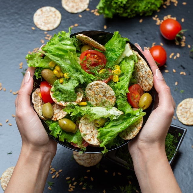 A vertical closeup of a person holding a bowl of salad with crackers and vegetables under the lights