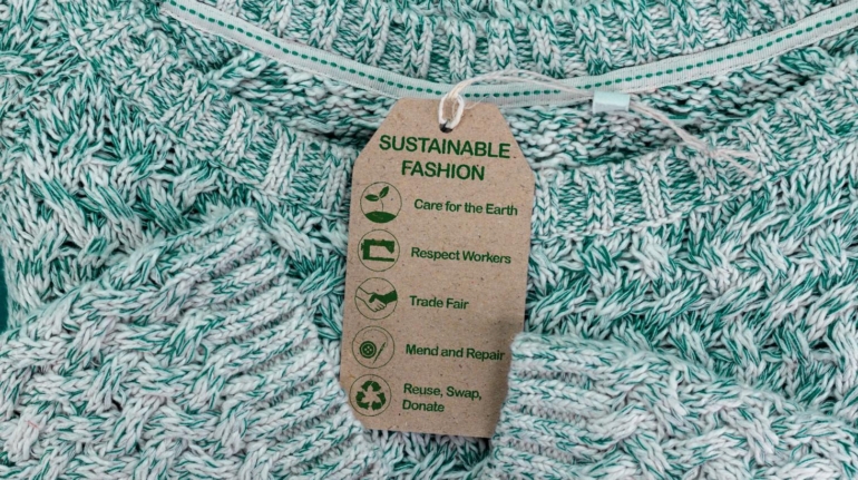 Un montón de jerséis grises con una etiqueta en el medio que dice sustainable fashion, o en español, moda sostenible.