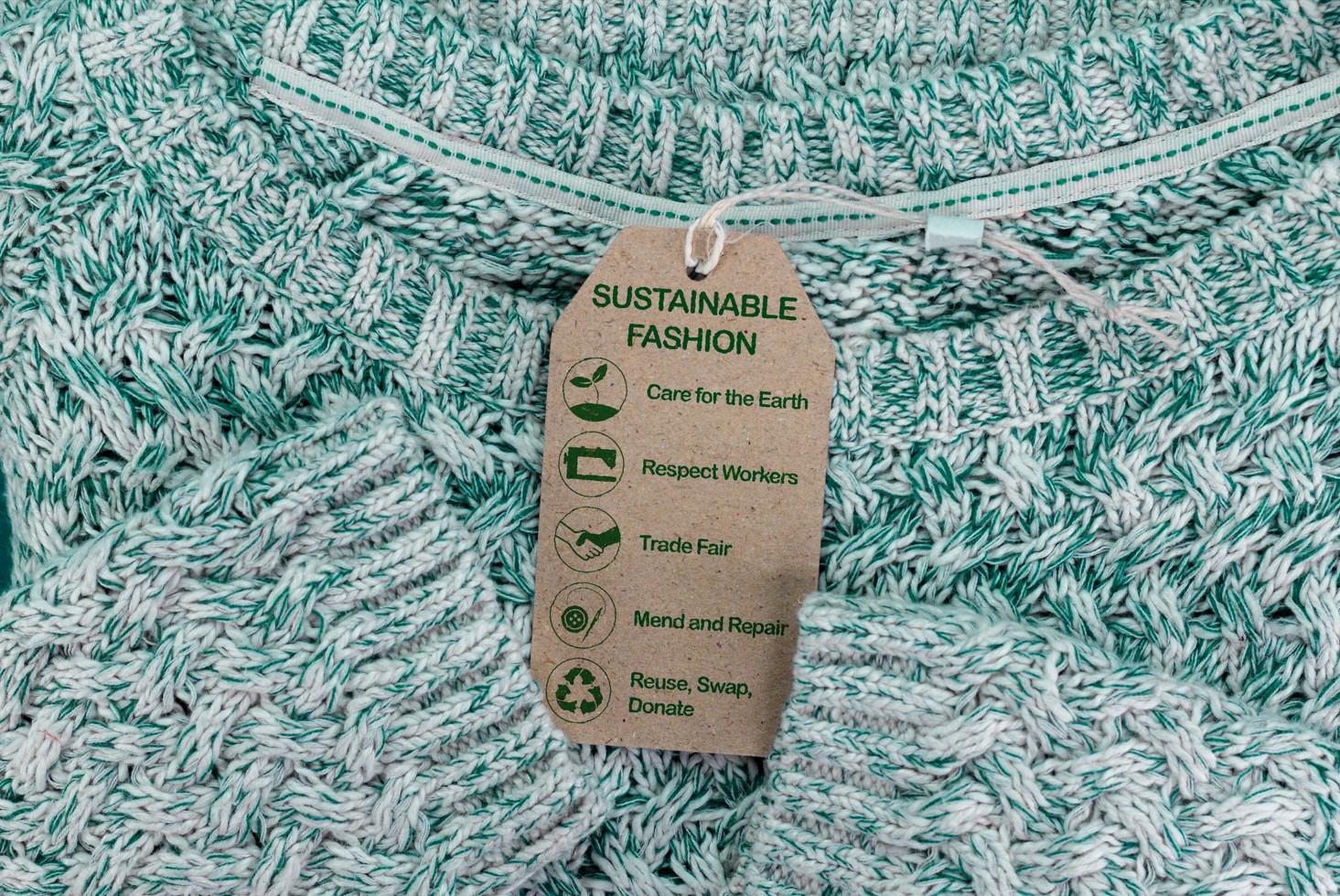 Un montón de jerséis grises con una etiqueta en el medio que dice sustainable fashion, o en español, moda sostenible. 
