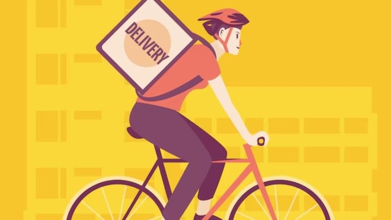 Un chico joven que lleva en la espalda una mochila de repartos pedaleando por la ciudad. Parece que está entregando pedidos en bicicleta.