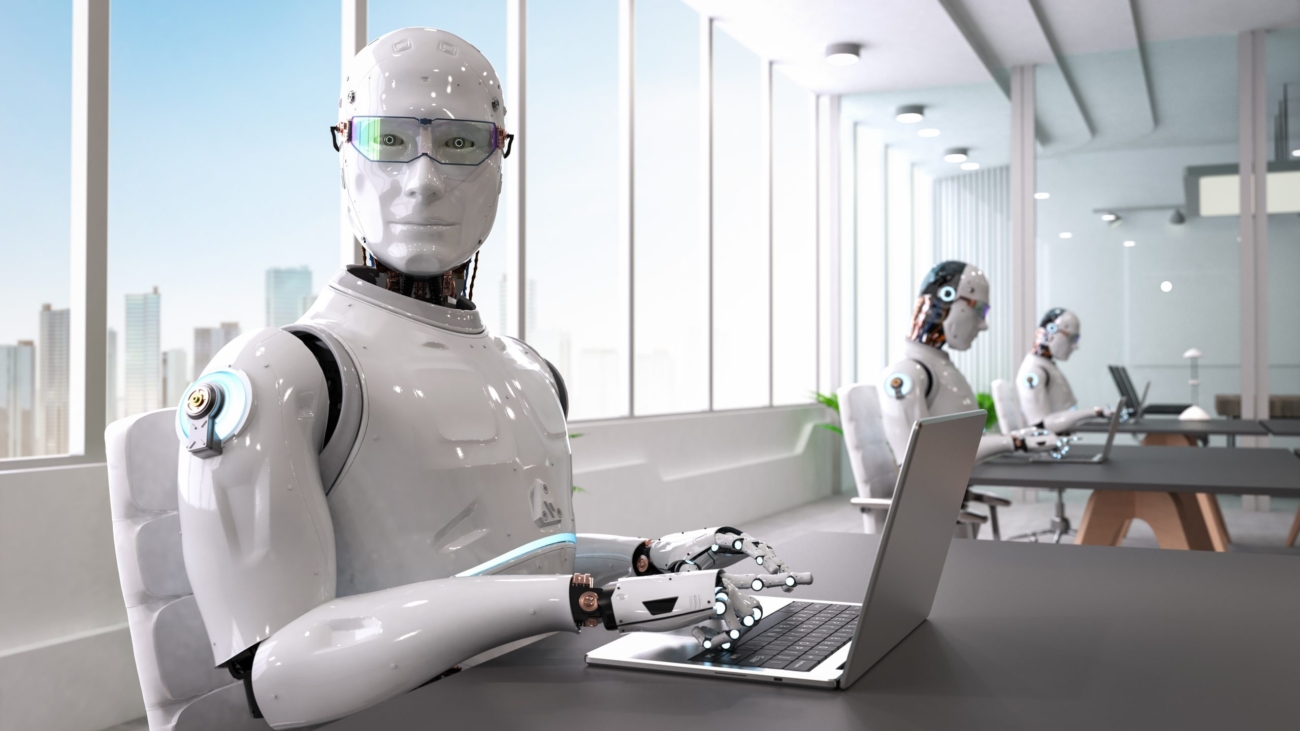 Un robot blanco con gafas que parece una persona trabajando en una oficina con un ordenador. Representa como las máquinas pueden quitarnos el trabajo (pista, si así lo hiciesen cavaríamos agujeros con las manos y no con retroexcavadoras)