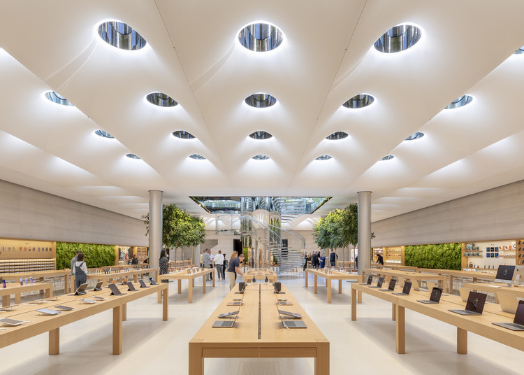 Una tienda super moderna de Apple con un decorado super guay. Las mesas son de madera, las paredes blancas y el techo tiene unas luces de apariencia futurística y una especie de techos arqueados. Se pueden ver reflejada con claridad su estrategia de marketing con valores.