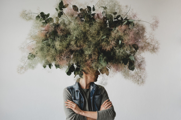 Large decorative bouquet made of green leaves and moss hangs over man's head