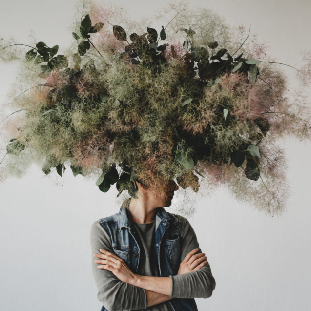 Large decorative bouquet made of green leaves and moss hangs over man's head